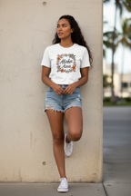 Woman wearing a white t-shirt with floral design and text, standing against a beige wall.